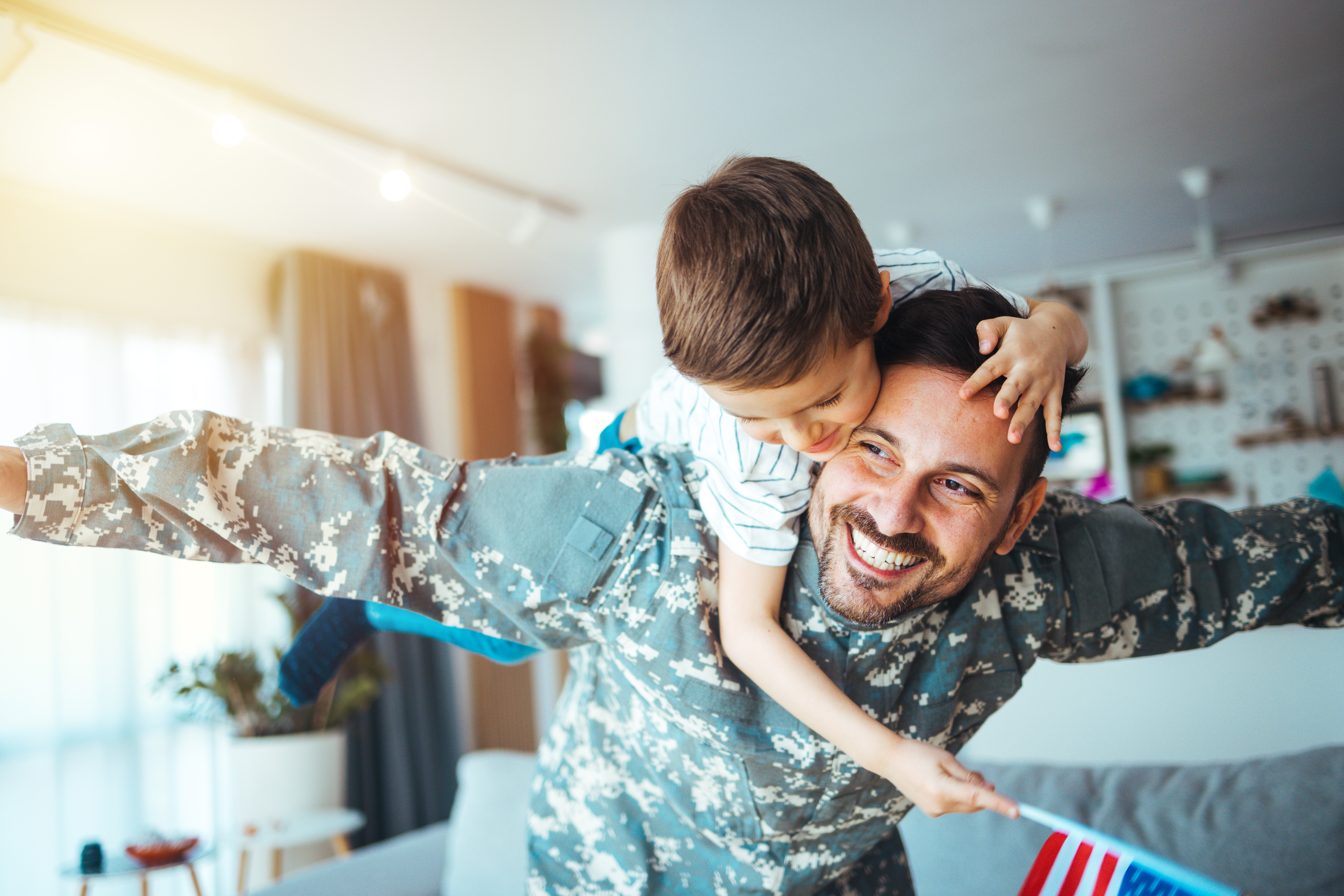 Soldier and his little son hugging at home. Smiling soldier reunited with his son after coming back from war. Military soldier father with son kid smiling during home return - Family love US army.