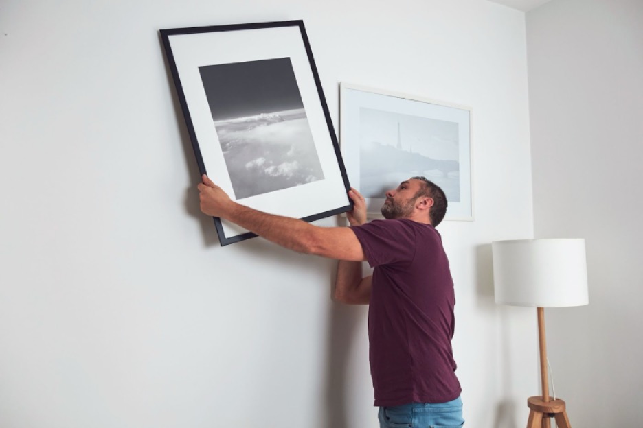 A person hanging a piece of art in his house.