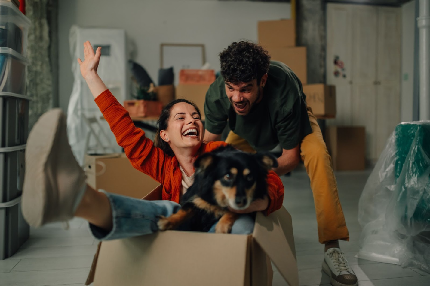 A couple and their dog moving into a home playing in a box.